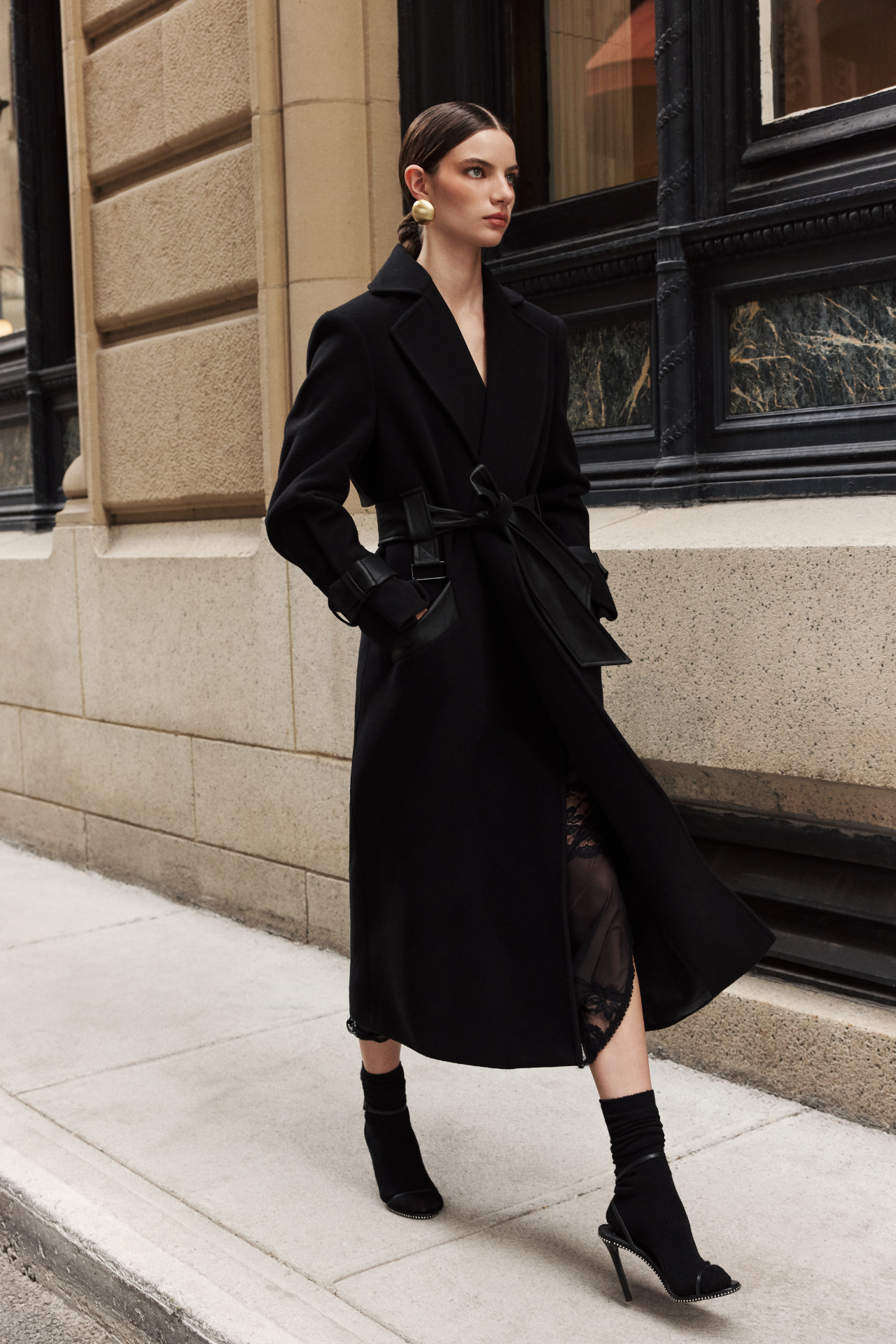 The EVERLY Black Wool Cashmere Blend Long Coat combines luxurious materials with structured, architectural design. Crafted from an Italian wool-cashmere blend, it features a leather tie belt at the waist to define the silhouette, along with structured shoulders and a classic notch collar. Leather cuff straps, a leather storm panel at the back, and single welt leather side pockets add refined detailing, while the back vent ensures ease of movement.