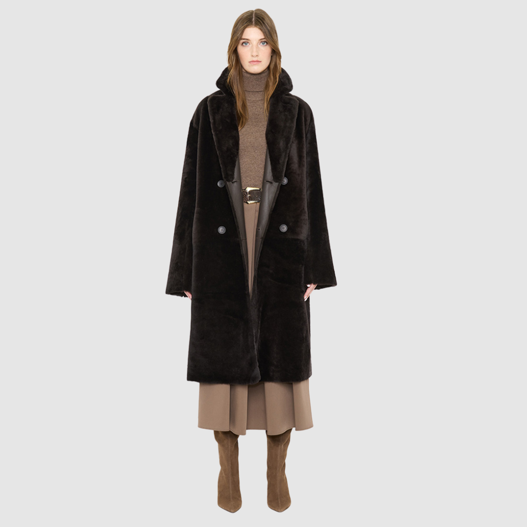 The ELLE Coat is a heritage-inspired oversized reversible shearling piece crafted in a chocolate nappa ironed wool teddy. Designed to transition seamlessly from smooth suede to plush wool-out texture, this versatile style blends timeless tailoring with modern après-ski elegance. A slight drop shoulder, double-breasted button closure, and back vent add structure to its oversized silhouette. Functional single welt pockets on the suede side and slash pockets on the ironed wool side
