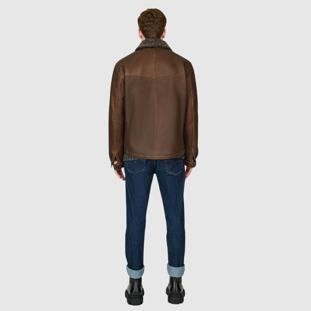 The PARRY Aged Bourbon Shearling Jacket delivers rugged refinement with a modern utilitarian edge. Crafted from semi-suede shearling, it features a semi-curly wool stand collar and a clean, semi-fitted silhouette through the shoulders, arms, and torso. Functional detailing includes chest patch pockets, sleeve button cuffs, and a mix of interior and exterior pockets for versatility. Finished with a single-breasted button closure, PARRY balances heritage shearling craftsmanship with contemporary shacket style
