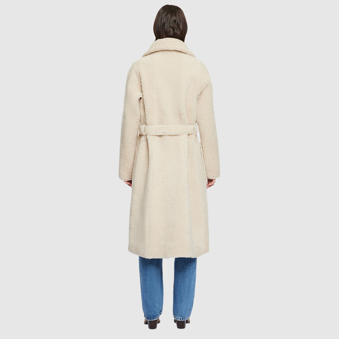 Introducing Zira, our vintage-inspired reversible nappa curly wool shearling coat. This elegant piece features a classic notch collar and effortlessly reverses to a cozy curly wool teddy. Designed with a relaxed dropped shoulder, 3-button closure, and a tie belt at the waist for a flattering fit, it offers both style and comfort. Practical zip pockets on the nappa side reverse to patch pockets on the teddy side, making Zira a versatile must-have for winter fashion.
