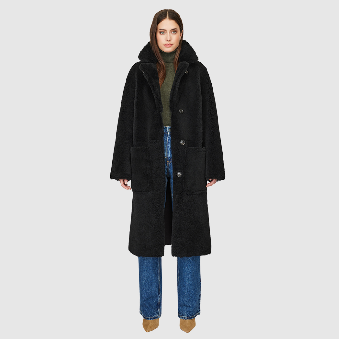 The HiSO Zira Grey Black Reversible Shearling features a vintage-inspired design, with a stylish suede curly wool on one side and cozy curly wool teddy on the other. It has a relaxed dropped shoulder and a three-button closure for a comfortable fit. The reversible nature of the jacket also includes a tie belt at the waist on the wool side and zip pockets on the suede side, while the teddy side has patch pockets.