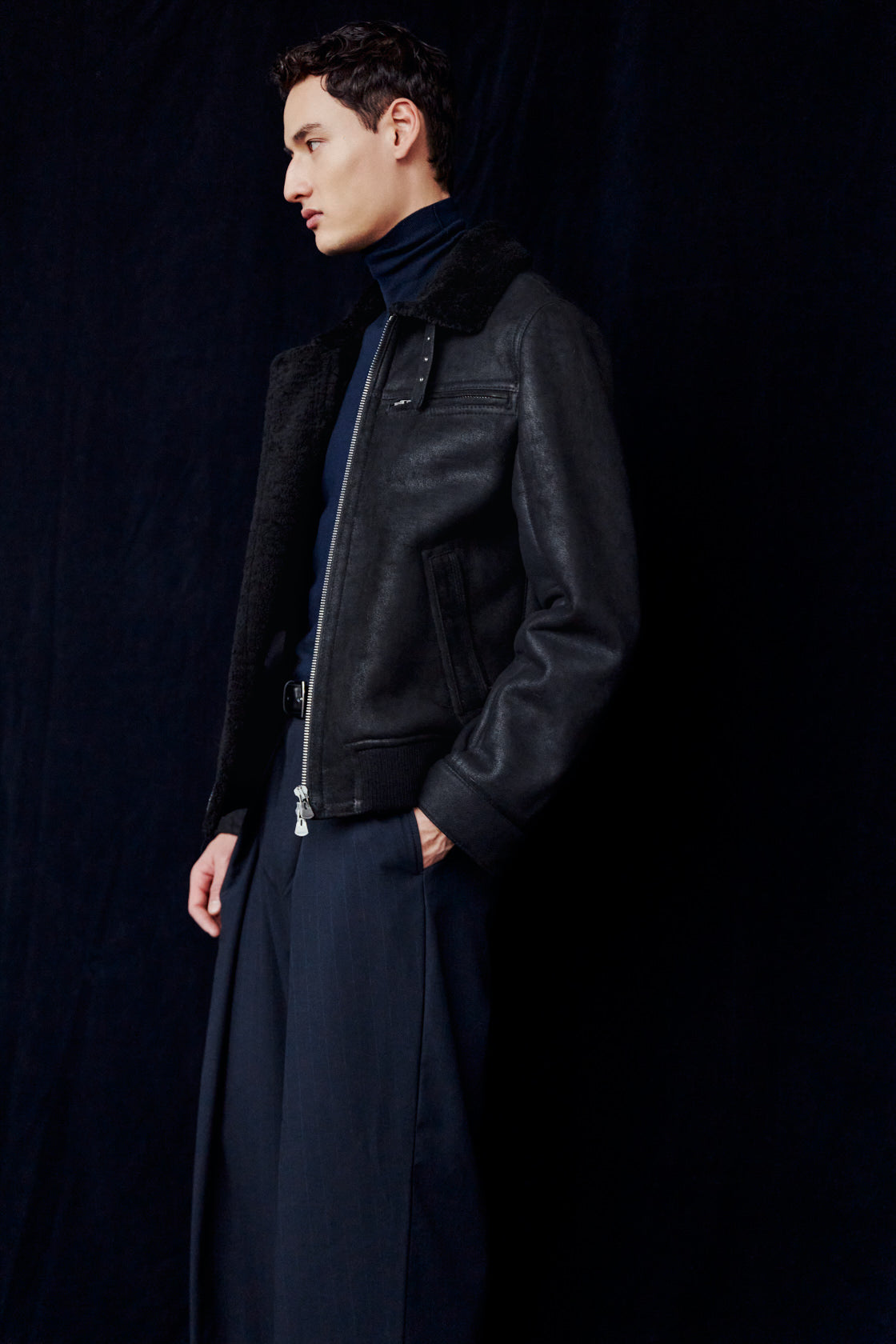The ARIES Jacket is a heritage-inspired shearling bomber crafted in jet black cracked nappa leather with plush curly wool on the interior. Designed for a regular-fit fit with regular shoulders, a convertible collar with an adjustable buckle strap, and a ribbed hemline, ARIES combines rugged edge with timeless texture. A functional horizontal zip chest pocket, welt side pockets, and a metallic front zip closure make this jacket as practical as it is versatile