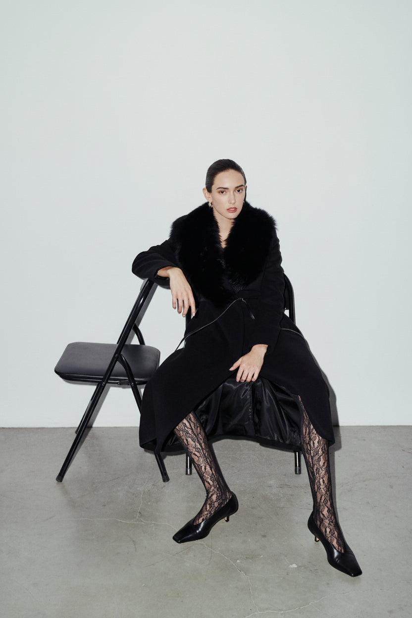 The ESTELLE Coat is a heritage-inspired full-length wool cashmere wrap coat crafted in deep jet black with a dramatic plush toscana wool shawl collar. Designed for a regular-fit fit with structured shoulders, a narrow leather tie belt, and a flared longline hem, ESTELLE combines modern edge with timeless texture. Functional welt side pockets and an open wrap front make this coat as practical as it is versatile, perfect for après-ski layering or elevated city styling.