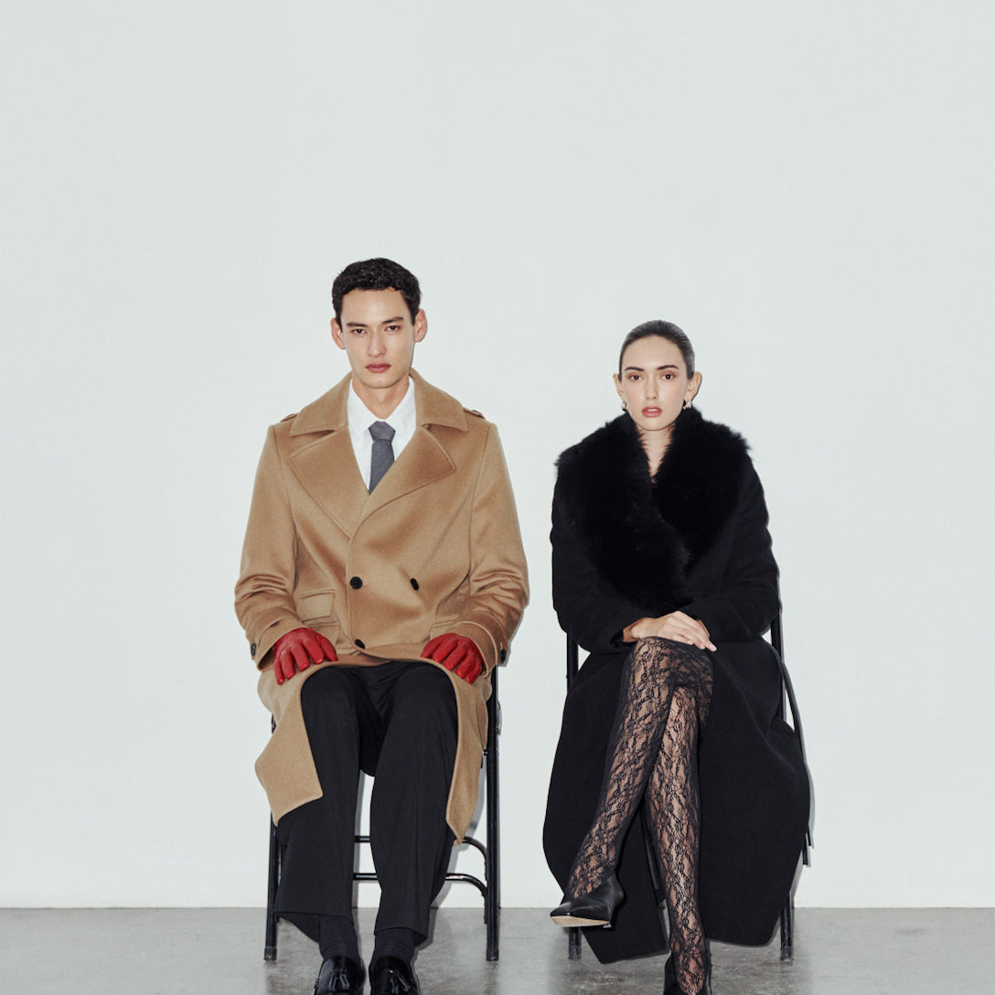 Tailored for timeless cold-weather style, the men's JOSEPH and women's ESTELLE coats combine classic structure with rich, luxurious materials. Crafted in rich camel wool,  JOSEPH brings a sharp, military-inspired edge with its longline double-breasted silhouette, structured shoulders, wide peaked lapels, shoulder epaulets, and functional flap pocketing. Complementing its masculine precision, the ESTELLE offers sweeping drama in deep jet-black wool-cashmere, featuring a plush Toscana wool shawl collar