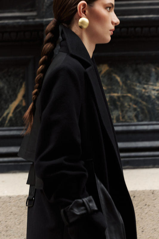 This sophisticated women's coat is a stylish wool trench coat featuring chic leather detail accents and distinctive sleeve straps. It boasts a classic notched collar. This elegant piece of outerwear offers a timeless silhouette. A perfect wool trench coat for a polished look.