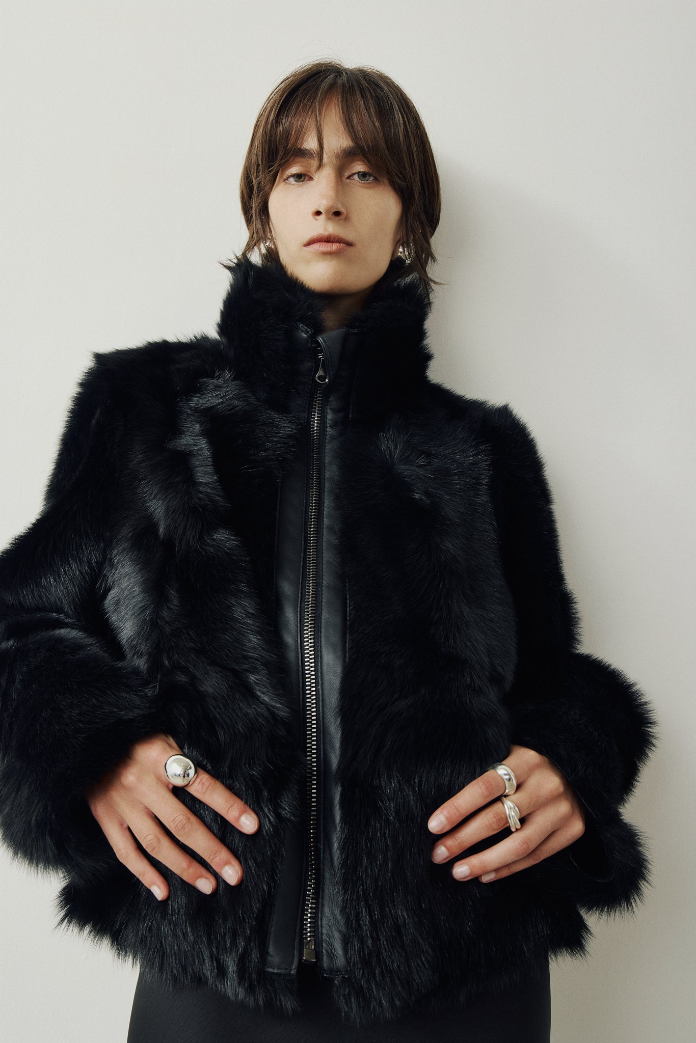 This cropped teddy jacket features a reversible design, with wool-out on one side and nappa-out on the other. The relaxed shoulder, spread collar, and slash side pockets provide comfort and functionality, while the front zip closure adds a practical touch.