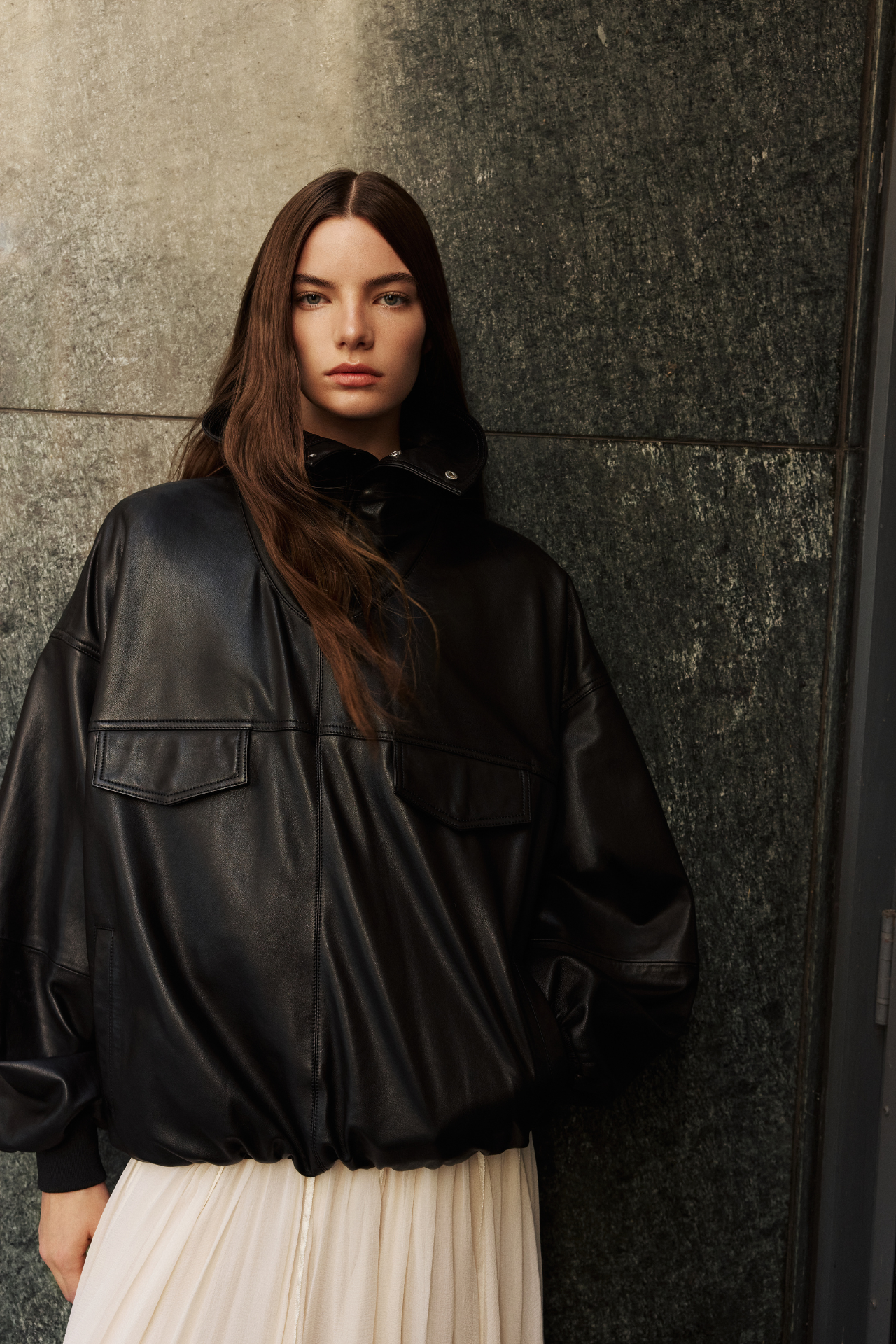 This stylish women's jacket is a chic piece of outerwear. Crafted from sleek leather, this coat features a modern, relaxed silhouette and a stand collar that can be worn up or folded down. It includes practical details such as front flap pockets and a gathered hem. This versatile leather jacket with its adaptable collar is perfect for adding an edgy yet sophisticated touch to any outfit. A must-have jacket for fashion-forward individuals seeking a contemporary coat option.