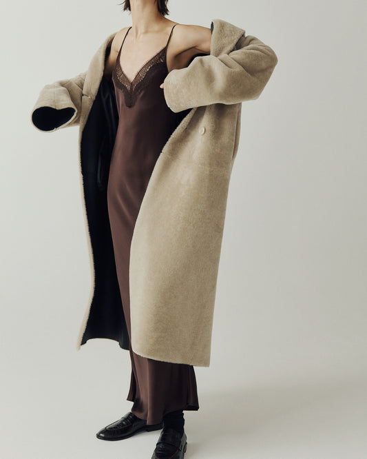 The DANIELLE Duster is a statement in heritage-inspired luxury and modern versatility. Crafted in black beige nappa and plush iron wool shearling, this reversible oversized coat transitions effortlessly from sleek leather to cozy teddy texture. Its elongated silhouette is enhanced with a slight drop shoulder, back vent, and double-breasted button closure, creating timeless elegance with functional edge. Practical single welt pockets on the suede side and slash pockets on the wool side
