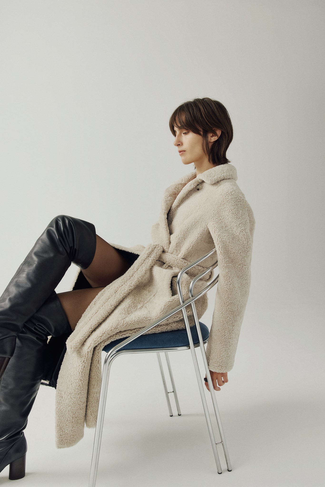 The EMBER Coat is a heritage-inspired wool-out curly mouton wrap crafted in rich black for timeless sophistication. Designed with a regular shoulder and fitted torso, it offers a flattering silhouette while maintaining comfort and warmth. A small curly wool notch collar, slash side pockets, and a front snap with tie belt closure combine function with elevated style. Fully lined for luxury, EMBER is perfect for après-ski evenings or refined everyday winter wear.