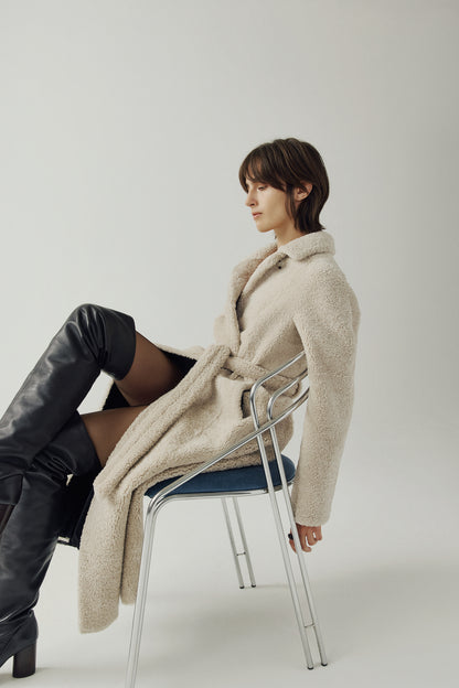 The EMBER Coat is a heritage-inspired wool-out curly mouton wrap crafted in rich black for timeless sophistication. Designed with a regular shoulder and fitted torso, it offers a flattering silhouette while maintaining comfort and warmth. A small curly wool notch collar, slash side pockets, and a front snap with tie belt closure combine function with elevated style. Fully lined for luxury, EMBER is perfect for après-ski evenings or refined everyday winter wear.