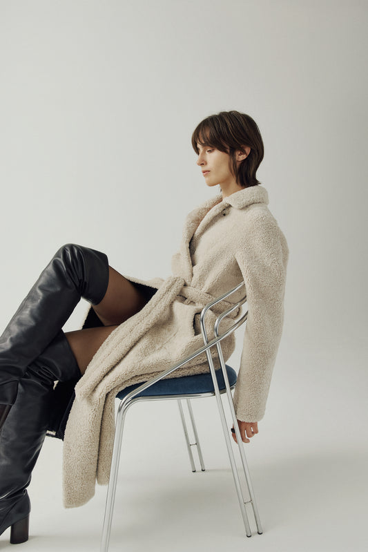 The EMBER Coat is a heritage-inspired wool-out curly mouton wrap crafted in rich black for timeless sophistication. Designed with a regular shoulder and fitted torso, it offers a flattering silhouette while maintaining comfort and warmth. A small curly wool notch collar, slash side pockets, and a front snap with tie belt closure combine function with elevated style. Fully lined for luxury, EMBER is perfect for après-ski evenings or refined everyday winter wear.