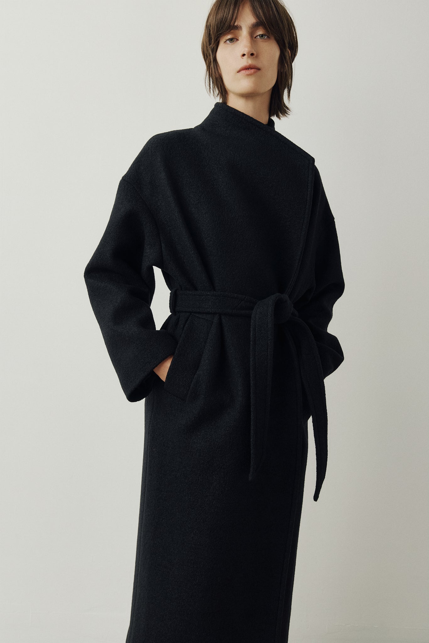 The Petra Taupe Boiled Wool Coat is crafted from premium Italian boiled wool, offering warmth, structure, and effortless sophistication. Designed as an oversized wrap silhouette, it features a tie belt for adjustable styling, drop shoulders for a relaxed drape, and a modern stand collar. Finished with discreet single welt side pockets, this coat balances timeless tailoring with contemporary ease—perfect for versatile cold-weather layering.