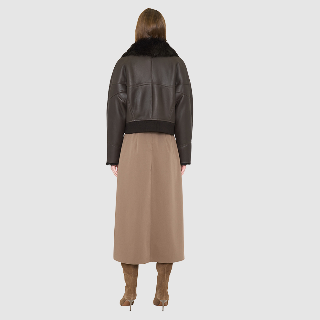 The CLARITY shearling bomber jacket offers a modern take on the classic bomber jacket, combining rugged function with luxurious texture. Crafted in a rich chocolate brown nappa leather and plush, dark rasado shearling wool interior, it delivers an elevated cold-weather look. Designed with a drop shoulder and a high shearling collar, it balances structure with relaxed ease. A tonal ribbed knit waistband, structural paneling, and clean hardware details lend utility to this elegant semi-fitted style
