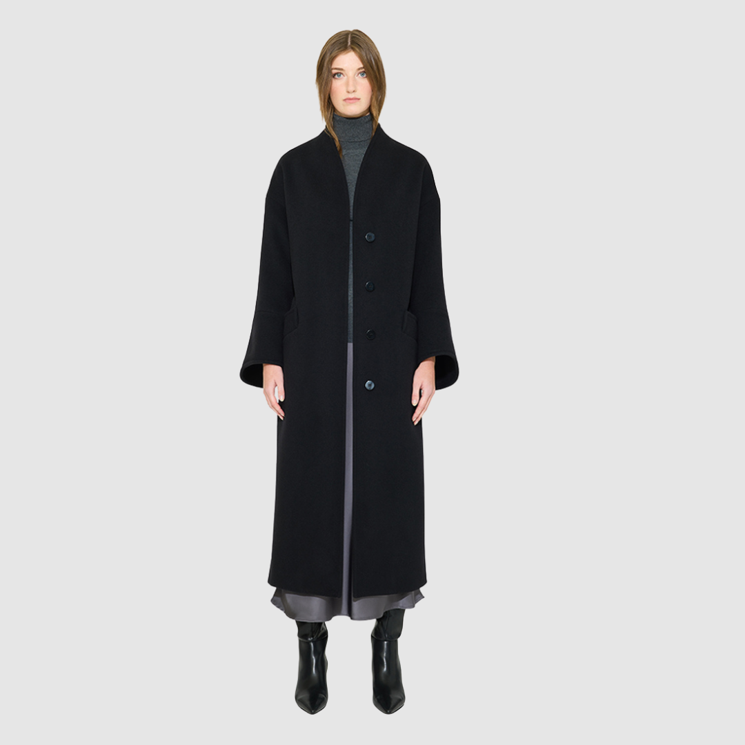 The LEONA Coat is a modern full-length silhouette crafted in a premium black wool blend. Designed with drop shoulders, wide kimono-inspired sleeves, and an easy, relaxed drape, it delivers effortless volume and architectural lines. A clean collarless V-neckline and single-breasted button closure give it a sleek, minimalist finish, while a matching tie belt and elasticized back waist offer versatile styling. Fully lined for comfort, LEONA serves as a definitive statement coat for elevated cold-weather 