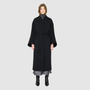 The LEONA Coat is a modern full-length silhouette crafted in a premium black wool blend. Designed with drop shoulders, wide kimono-inspired sleeves, and an easy, relaxed drape, it delivers effortless volume and architectural lines. A clean collarless V-neckline and single-breasted button closure give it a sleek, minimalist finish, while a matching tie belt and elasticized back waist offer versatile styling. Fully lined for comfort, LEONA serves as a definitive statement coat for elevated cold-weather 