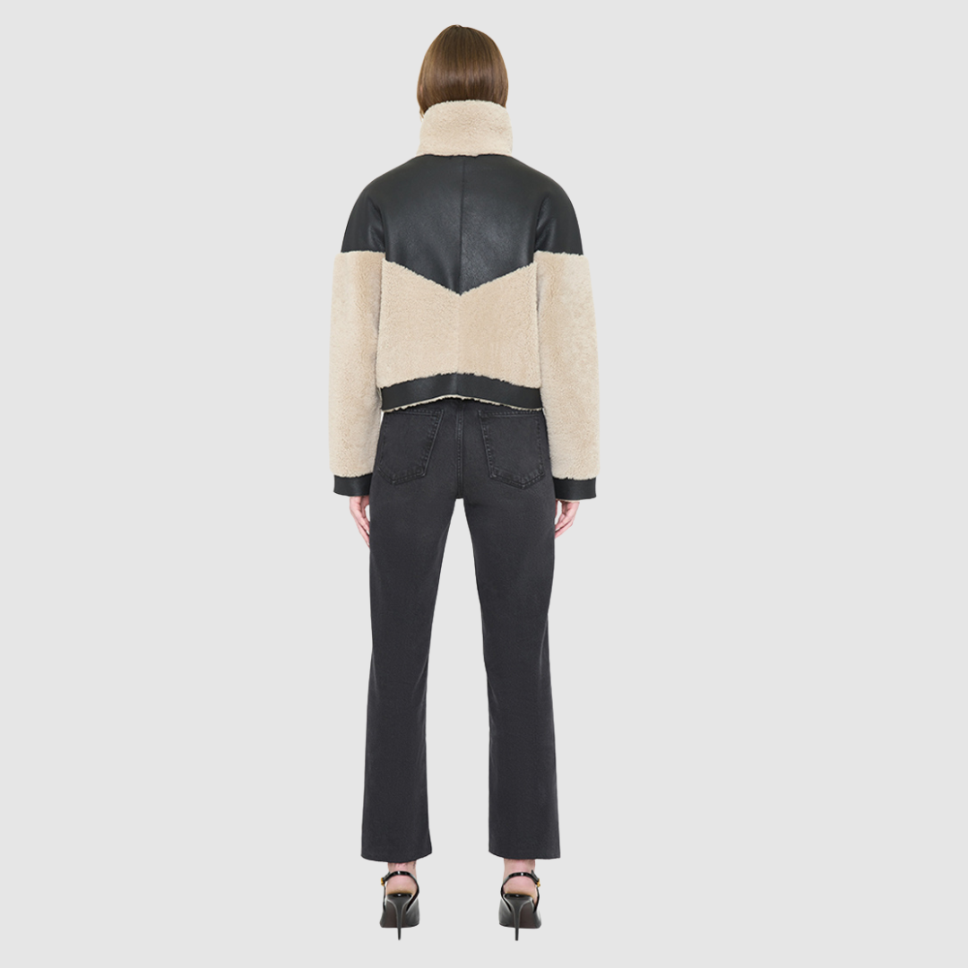 The LILITH Jacket is a heritage-inspired cropped shearling jacket crafted from black nappa leather with plush, contrasting beige wool detailing for modern texture and dimension. Its drop shoulder and relaxed cropped silhouette create a sleek, contemporary fit, while a dramatic chevron-blocked design across the chest, shoulders, and sleeves adds a striking graphic edge. Featuring a multi-functional front zip closure that deep side pockets, and exposed beige shearling trim at the cuffs and hem, LILITH is as p
