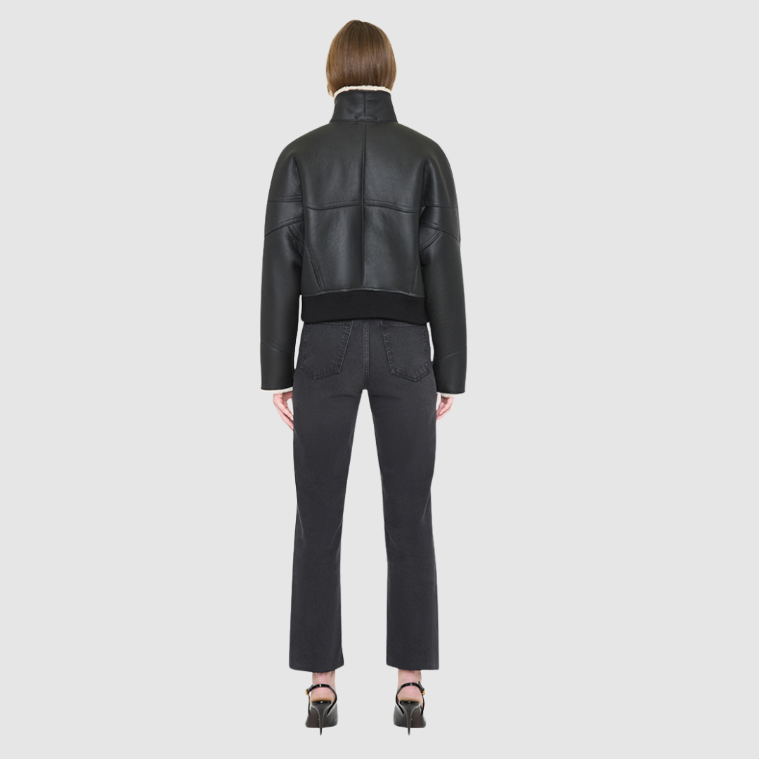 The LUMI Jacket is a heritage-inspired cropped shearling aviator crafted from black nappa leather and plush cream wool detailing for modern texture and dimension. Its regular shoulder and tailored cropped silhouette create a sleek, contemporary fit, while architectural paneled lines add a clean, minimalist edge. Functional exterior welt pockets, front zip closure, and a thick tonal ribbed knit waistband make LUMI as practical as it is stylish, perfect for après-ski layering or urban winter looks.