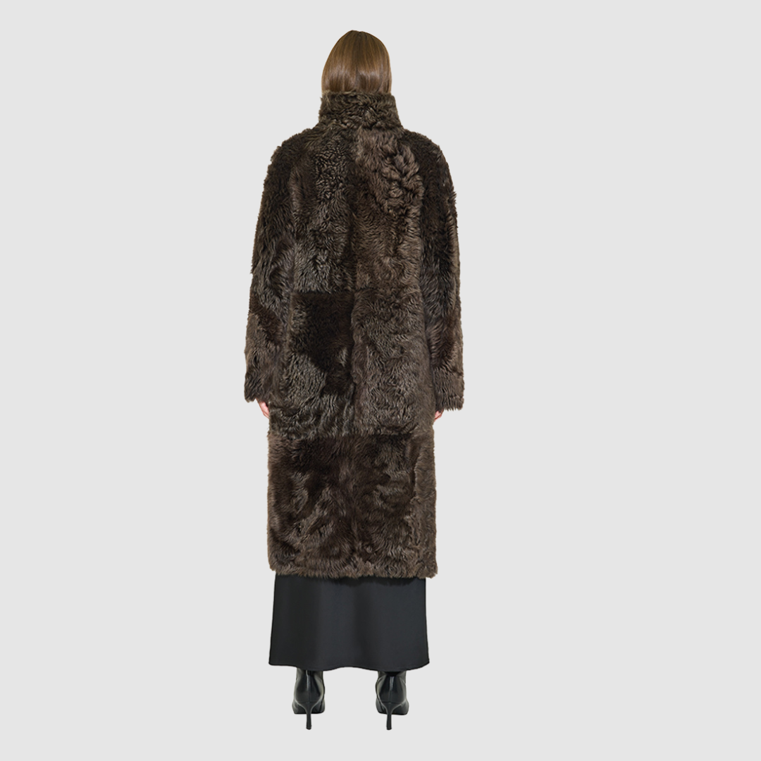 OMEGA introduces an element of understated luxury to cold-weather dressing, offering a longline silhouette engineered for seasonal transition. This exquisite investment outerwear piece pairs a deep carbon suede exterior skin with a rich, magnificent semi curly toscana wool teddy on the reverse side. Designed to shift seamlessly from a dramatic, texture-forward profile to a classic, minimalist skin-out aesthetic, this fully reversible coat adapts effortlessly to your outfit. 