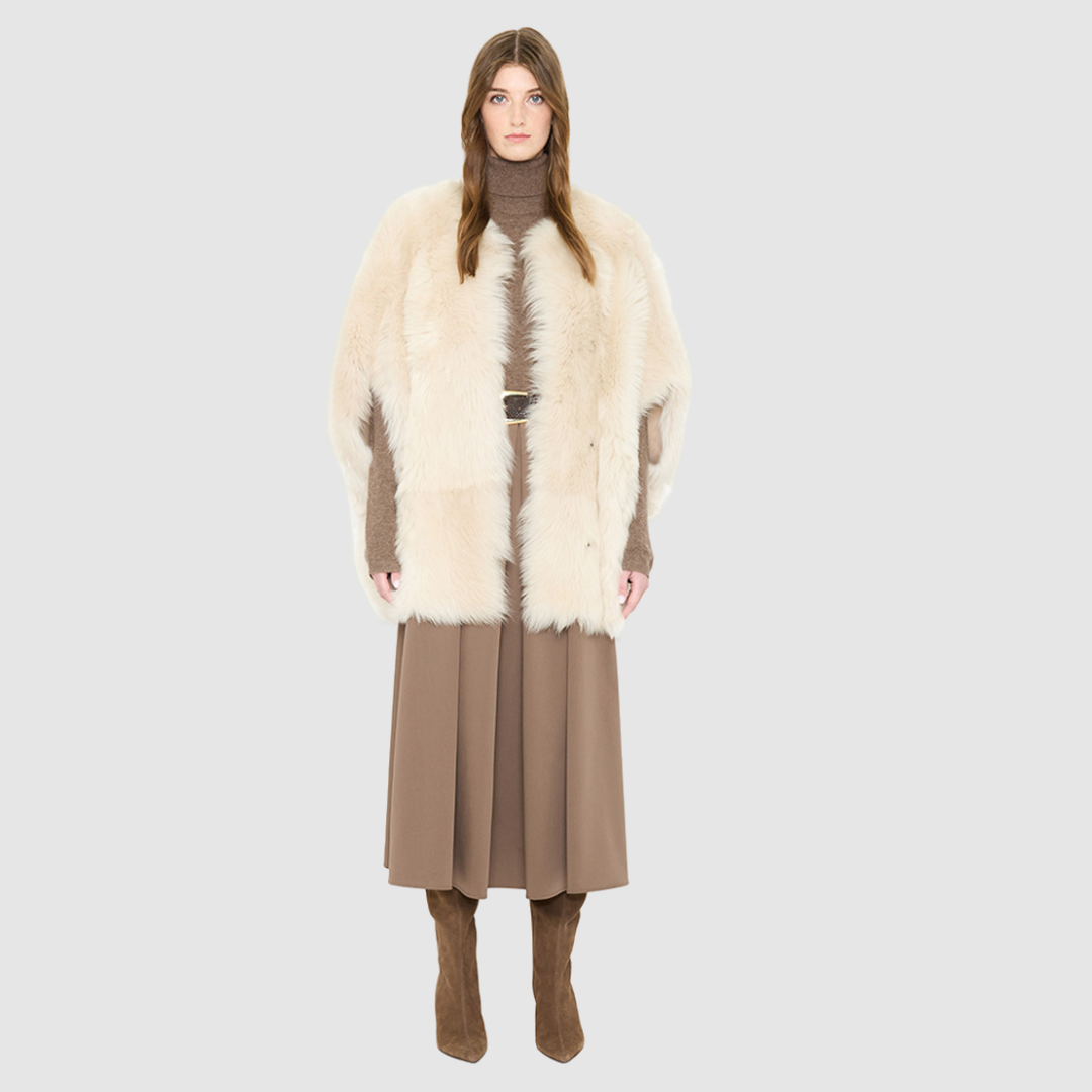 The ROTHEN Cocoon Vest is a modern oversized silhouette crafted in luxurious parchment-toned toscana wool. Designed with a generous drop shoulder and a relaxed, fluid drape, it delivers effortless volume and architectural style. A collarless neckline and discrete button closure give it a clean, minimalist finish, while a fully reversible design shifts from a suede side to a plush toscana teddy side for versatile styling. Providing ultimate natural insulation, ROTHEN is the ultimate statement piece for eleva