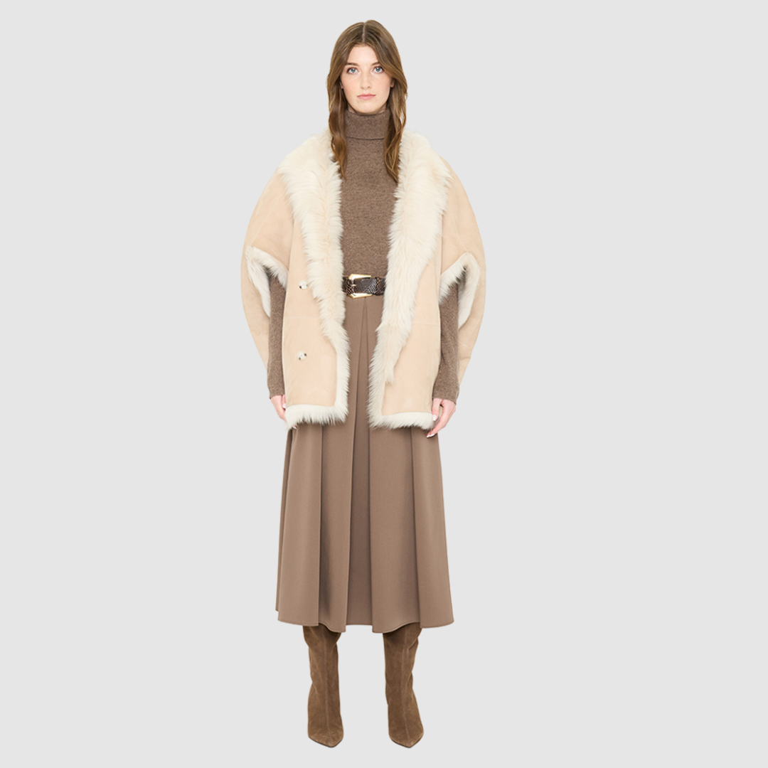 The ROTHEN Cocoon Vest is a modern oversized silhouette crafted in luxurious parchment-toned toscana wool. Designed with a generous drop shoulder and a relaxed, fluid drape, it delivers effortless volume and architectural style. A collarless neckline and discrete button closure give it a clean, minimalist finish, while a fully reversible design shifts from a suede side to a plush toscana teddy side for versatile styling. Providing ultimate natural insulation, ROTHEN is the ultimate statement piece for eleva