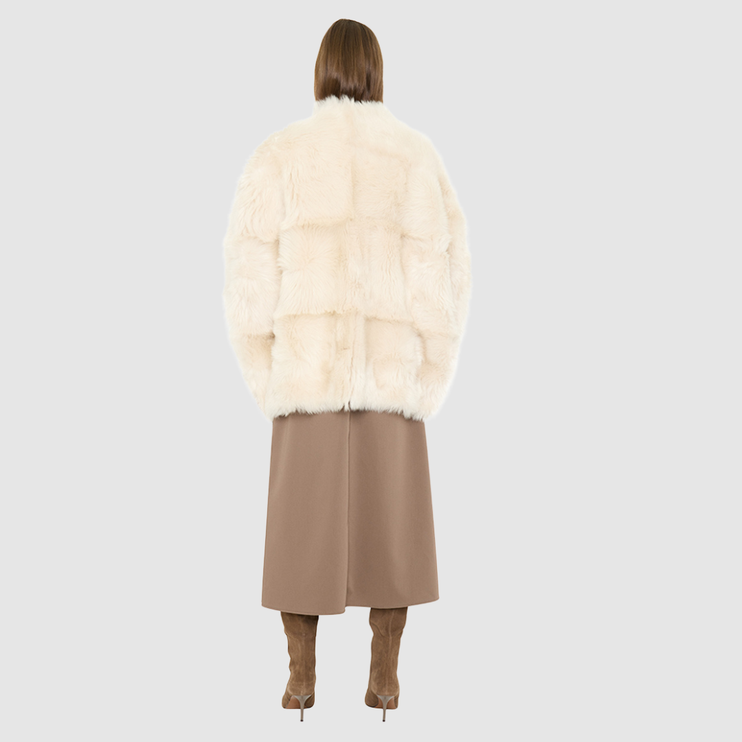 The ROTHEN Cocoon Vest is a modern oversized silhouette crafted in luxurious parchment-toned toscana wool. Designed with a generous drop shoulder and a relaxed, fluid drape, it delivers effortless volume and architectural style. A collarless neckline and discrete button closure give it a clean, minimalist finish, while a fully reversible design shifts from a suede side to a plush toscana teddy side for versatile styling. Providing ultimate natural insulation, ROTHEN is the ultimate statement piece for eleva