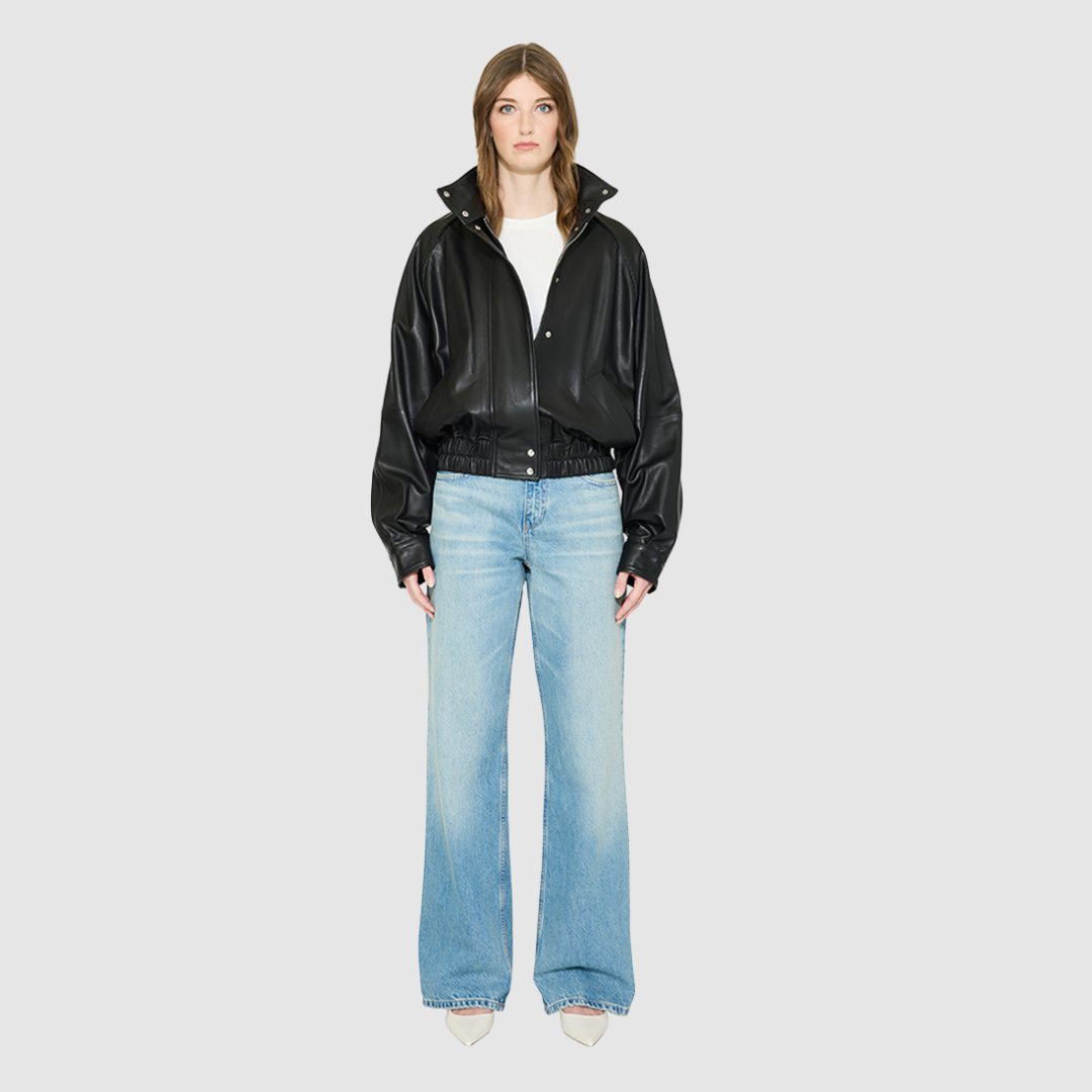 The WREN Bomber Jacket is a modern silhouette crafted in supple black nappa leather. Designed with raglan drop shoulders and an easy, relaxed volume through the body, it delivers sharp architectural presence with a sporty edge. A high stand funnel collar and concealed front zip closure with snap storm placket give it a clean, minimalist finish, while a gathered elasticized leather hem defines the waist. Fully lined for comfort, WREN serves as a definitive statement piece for transitional and cold-weather