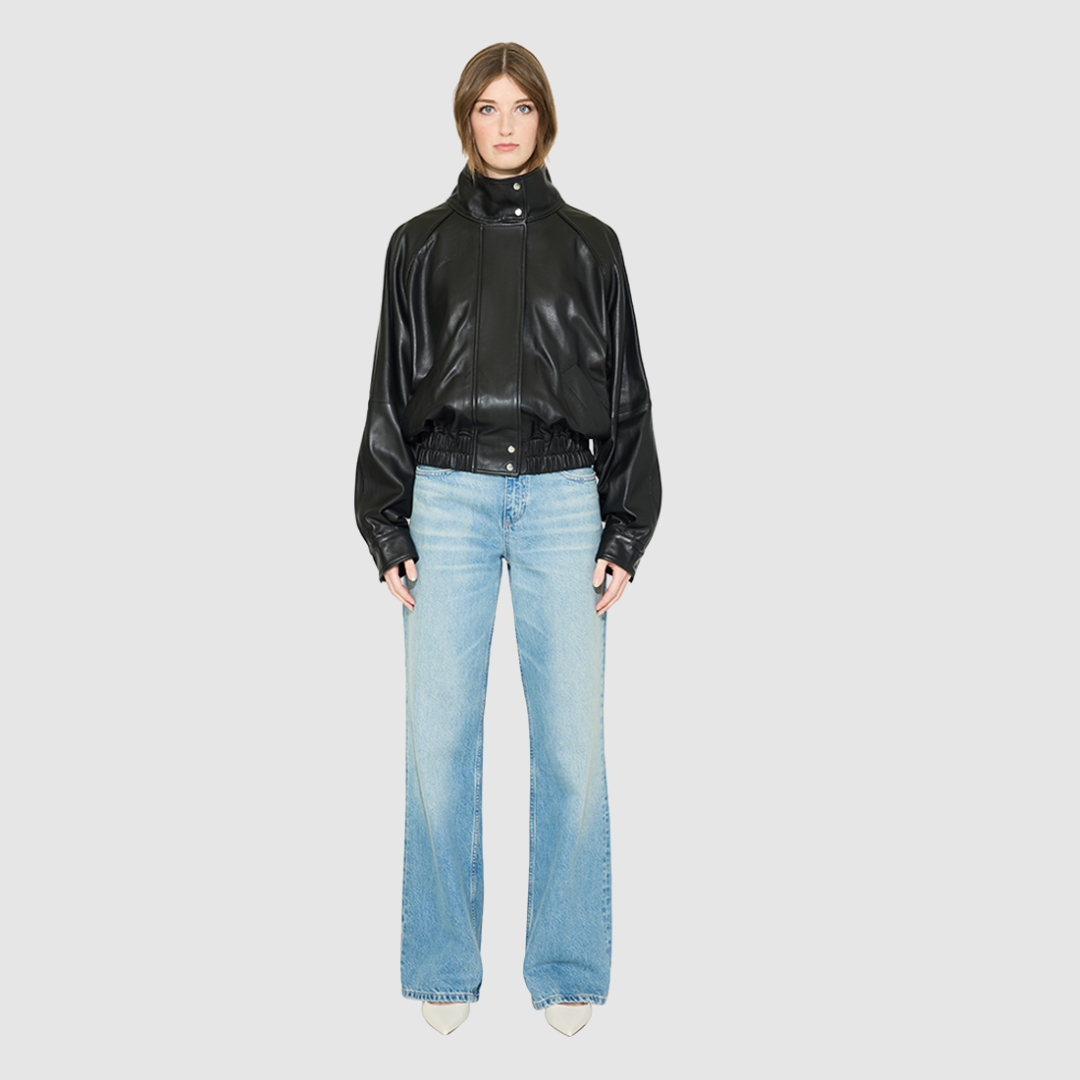 The WREN Bomber Jacket is a modern silhouette crafted in supple black nappa leather. Designed with raglan drop shoulders and an easy, relaxed volume through the body, it delivers sharp architectural presence with a sporty edge. A high stand funnel collar and concealed front zip closure with snap storm placket give it a clean, minimalist finish, while a gathered elasticized leather hem defines the waist. Fully lined for comfort, WREN serves as a definitive statement piece for transitional and cold-weather