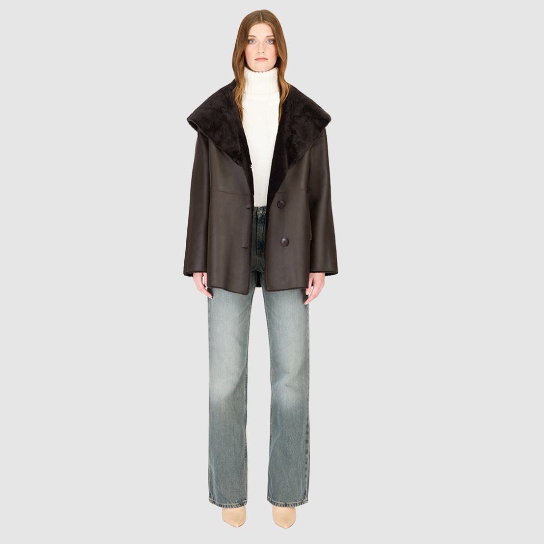 The CHEREZ Jacket is a modern mid-length hooded silhouette crafted in chocolate nappa leather shearling. Designed with drop shoulders, it offers dual-fit versatility with a tailored regular fit on the nappa side and a relaxed fit when reversed to the plush wool-out side. An exaggerated convertible hood drapes effortlessly across the shoulders as a shawl-like collar when unbuttoned, while a single-breasted button closure delivers a clean, minimalist finish. 