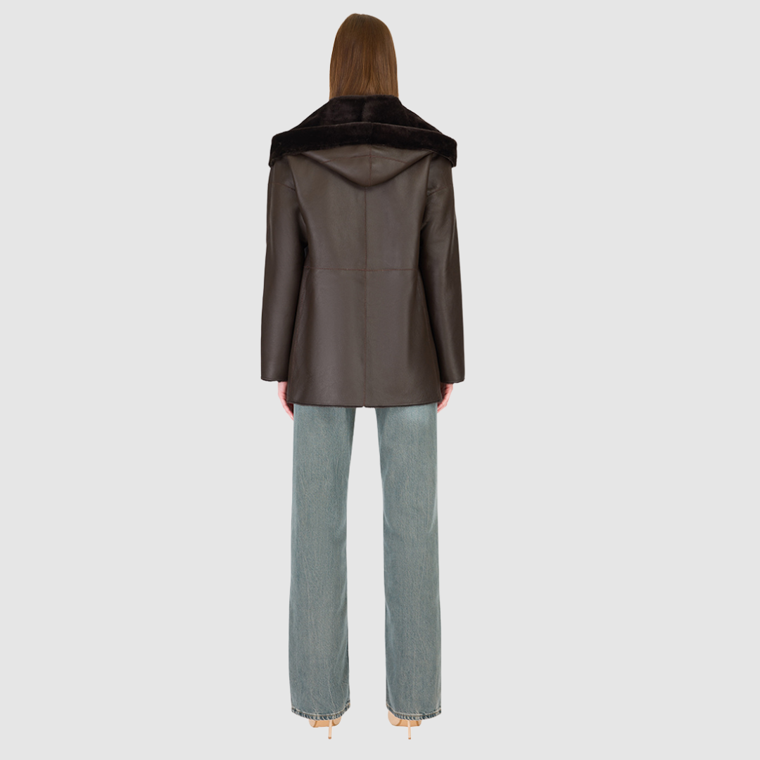 The CHEREZ Jacket is a modern mid-length hooded silhouette crafted in chocolate nappa leather shearling. Designed with drop shoulders, it offers dual-fit versatility with a tailored regular fit on the nappa side and a relaxed fit when reversed to the plush wool-out side. An exaggerated convertible hood drapes effortlessly across the shoulders as a shawl-like collar when unbuttoned, while a single-breasted button closure delivers a clean, minimalist finish. 