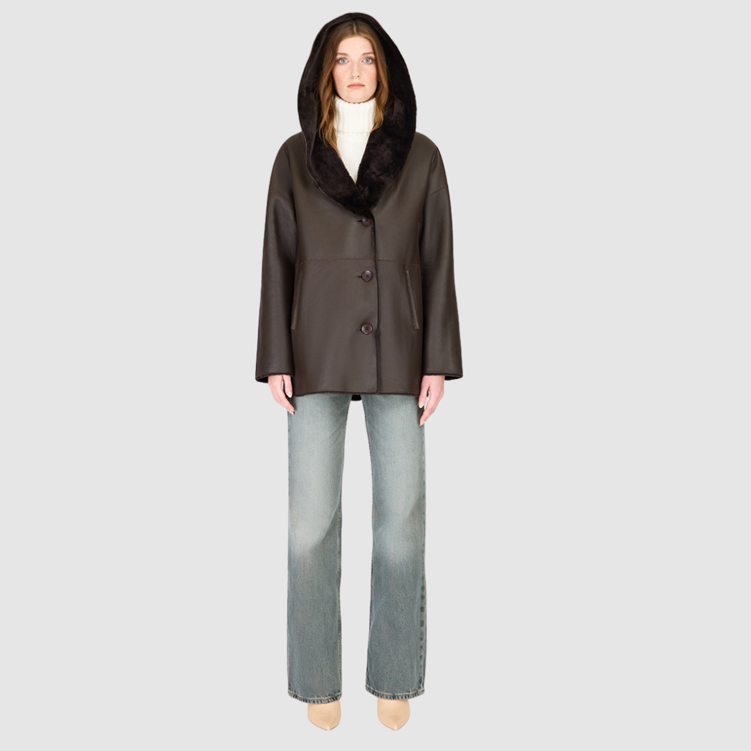The CHEREZ Jacket is a modern mid-length hooded silhouette crafted in chocolate nappa leather shearling. Designed with drop shoulders, it offers dual-fit versatility with a tailored regular fit on the nappa side and a relaxed fit when reversed to the plush wool-out side. An exaggerated convertible hood drapes effortlessly across the shoulders as a shawl-like collar when unbuttoned, while a single-breasted button closure delivers a clean, minimalist finish. 