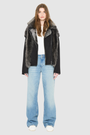 The INDIRA Shearling Jacket offers a modern take on the classic moto jacket, combining rugged function with luxurious texture. Crafted in a rich black suede that features a plush, long-haired grey Toscana shearling wool interior, it delivers an elevated cold-weather look. Designed with a distinct drop shoulder and a relaxed silhouette, it balances structure with effortless ease. Striking exposed toscana wool panels cascade down the center back and frame the front closure.