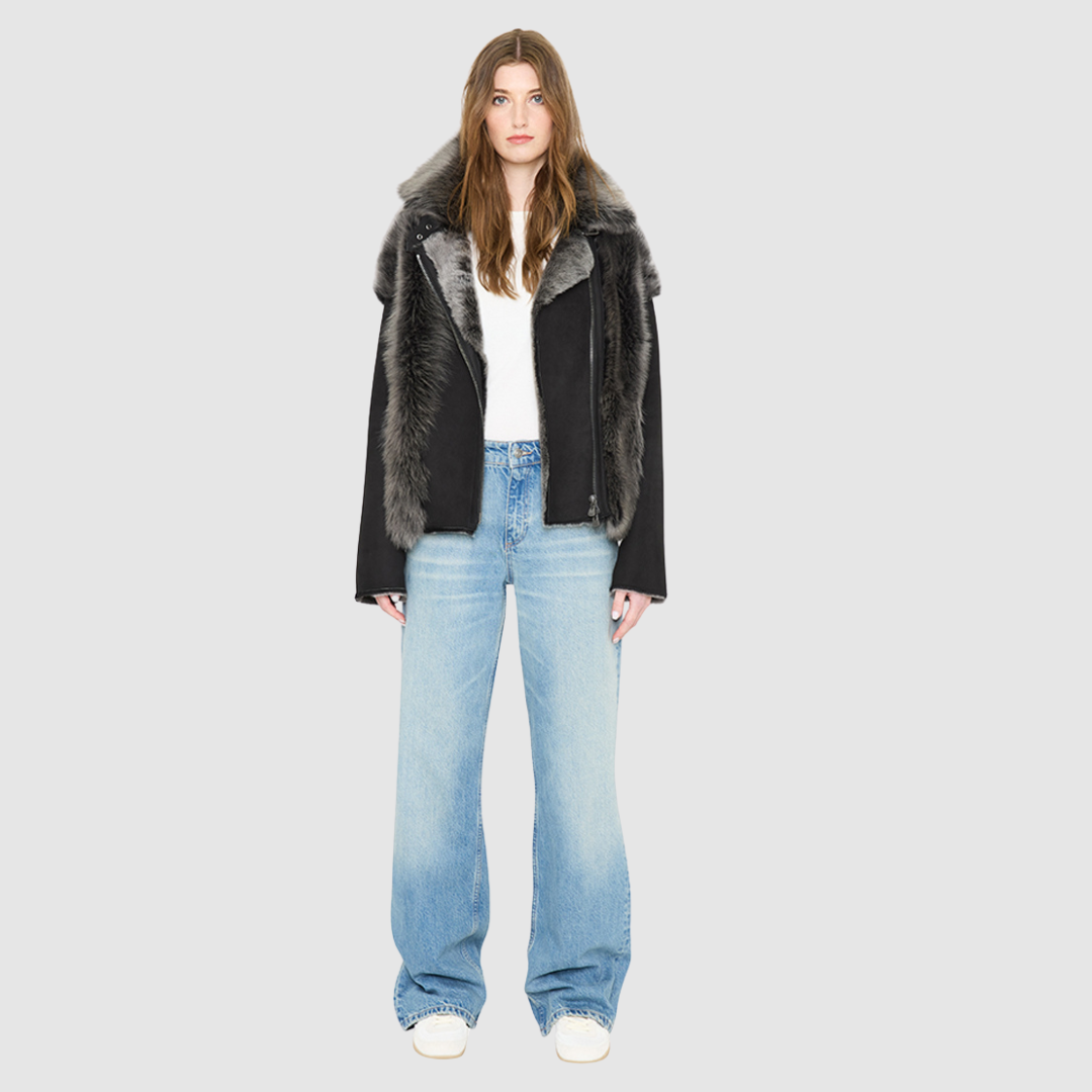 The INDIRA Shearling Jacket offers a modern take on the classic moto jacket, combining rugged function with luxurious texture. Crafted in a rich black suede that features a plush, long-haired grey Toscana shearling wool interior, it delivers an elevated cold-weather look. Designed with a distinct drop shoulder and a relaxed silhouette, it balances structure with effortless ease. Striking exposed toscana wool panels cascade down the center back and frame the front closure.