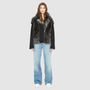 The INDIRA Shearling Jacket offers a modern take on the classic moto jacket, combining rugged function with luxurious texture. Crafted in a rich black suede that features a plush, long-haired grey Toscana shearling wool interior, it delivers an elevated cold-weather look. Designed with a distinct drop shoulder and a relaxed silhouette, it balances structure with effortless ease. Striking exposed toscana wool panels cascade down the center back and frame the front closure.