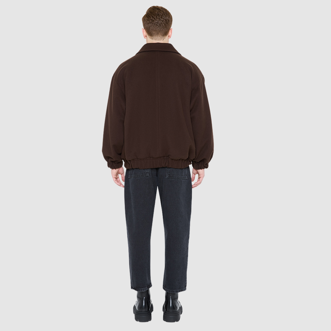 The MALCOLM Bomber Jacket is a modern silhouette crafted in a rich chocolate brown wool blend. Designed with drop shoulders and an easy, relaxed volume through the body, it delivers architectural presence and effortless style. A high convertible spread collar and two-way front zip closure give it a clean, minimalist finish, while oversized front flap patch pockets and elasticized cuffs and hem define the shape. Fully lined for comfort, MALCOLM serves as a definitive statement piece for cold-weather layering