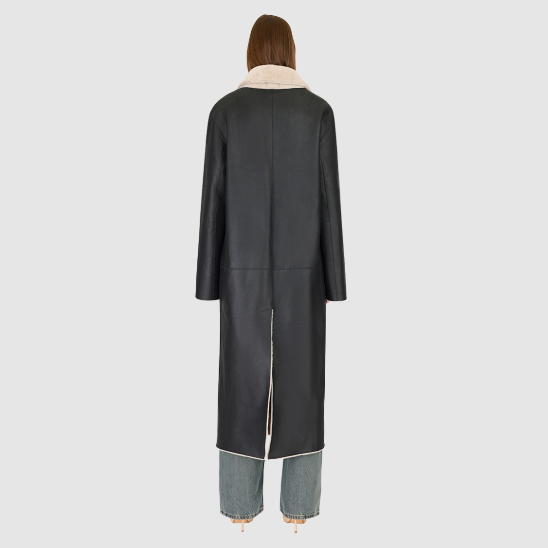The DANIELLE Duster is a statement in heritage-inspired luxury and modern versatility. Crafted in black beige nappa and plush iron wool shearling, this reversible oversized coat transitions effortlessly from sleek leather to cozy teddy texture. Its elongated silhouette is enhanced with a slight drop shoulder, back vent, and double-breasted button closure, creating timeless elegance with functional edge. Practical single welt pockets on the suede side and slash pockets on the wool side