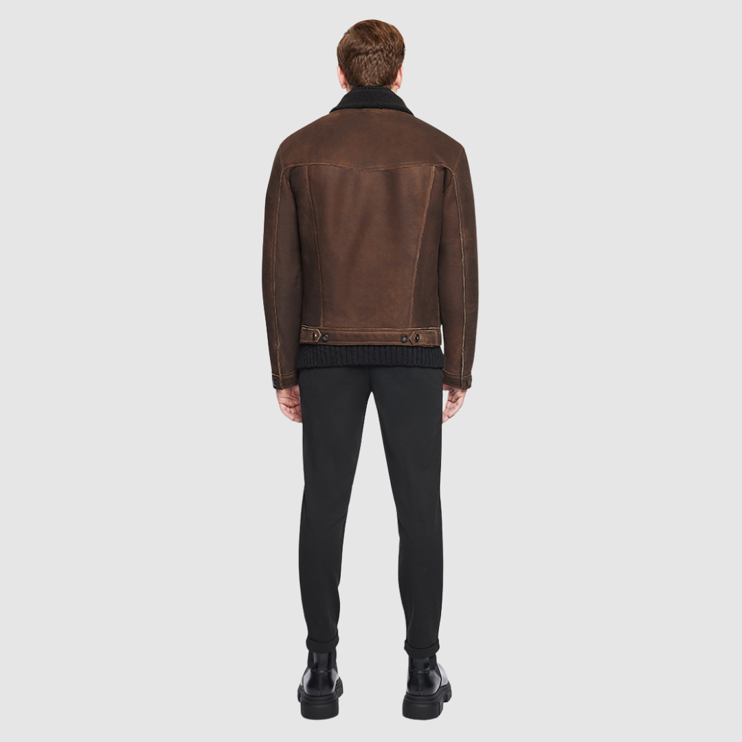 The Leary aged bourbon shearling jacket channels classic menswear tailoring through the lens of rugged luxury. Crafted from rich semi suede and finished with a curly wool notch collar, it offers a fitted silhouette through the shoulders and chest while maintaining ease of movement. Buttoned cuffs and chest pockets add a utilitarian edge, balanced by refined welt side pockets and a concealed interior pouch pocket. Finished with a clean front button closure. 