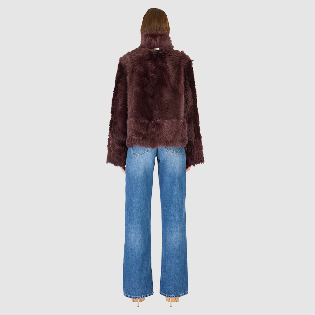 This cropped teddy jacket features a reversible design, with wool-out on one side and nappa-out on the other. The relaxed shoulder, spread collar, and slash side pockets provide comfort and functionality, while the front zip closure adds a practical touch.