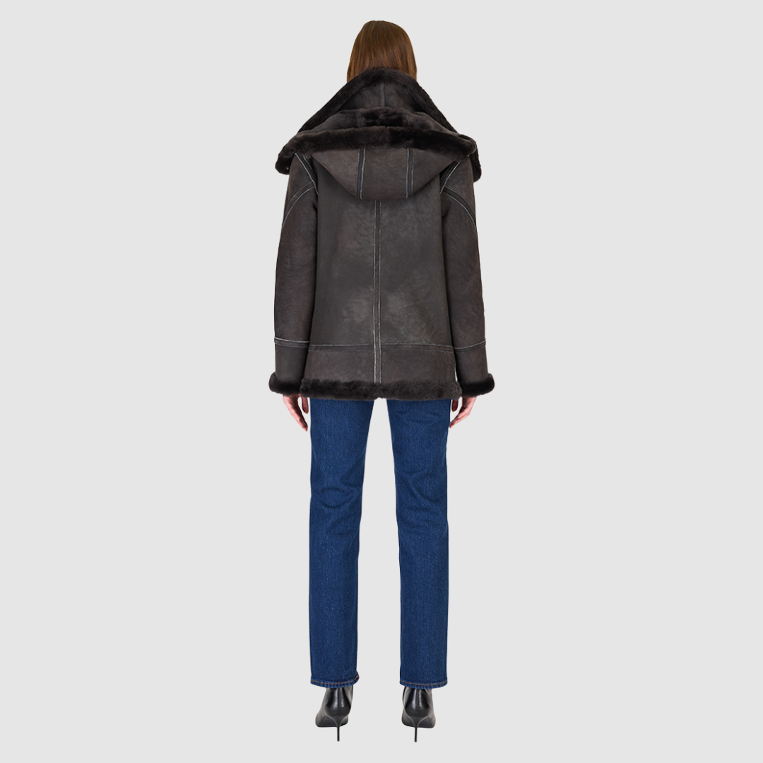 The MARTINA Jacket is a heritage-inspired medium-length shearling moto crafted in black vintage suede&nbsp;leather with curly wool collar and trims for elevated texture and warmth. Its relaxed fit with dropped shoulders ensures a modern, effortless silhouette, while the removable hood adds versatility for changing weather. Practical hidden interior pockets, exterior side zip pockets, and an asymmetrical front zip closure combine function with luxe design, making MARTINA ideal for après-ski layering