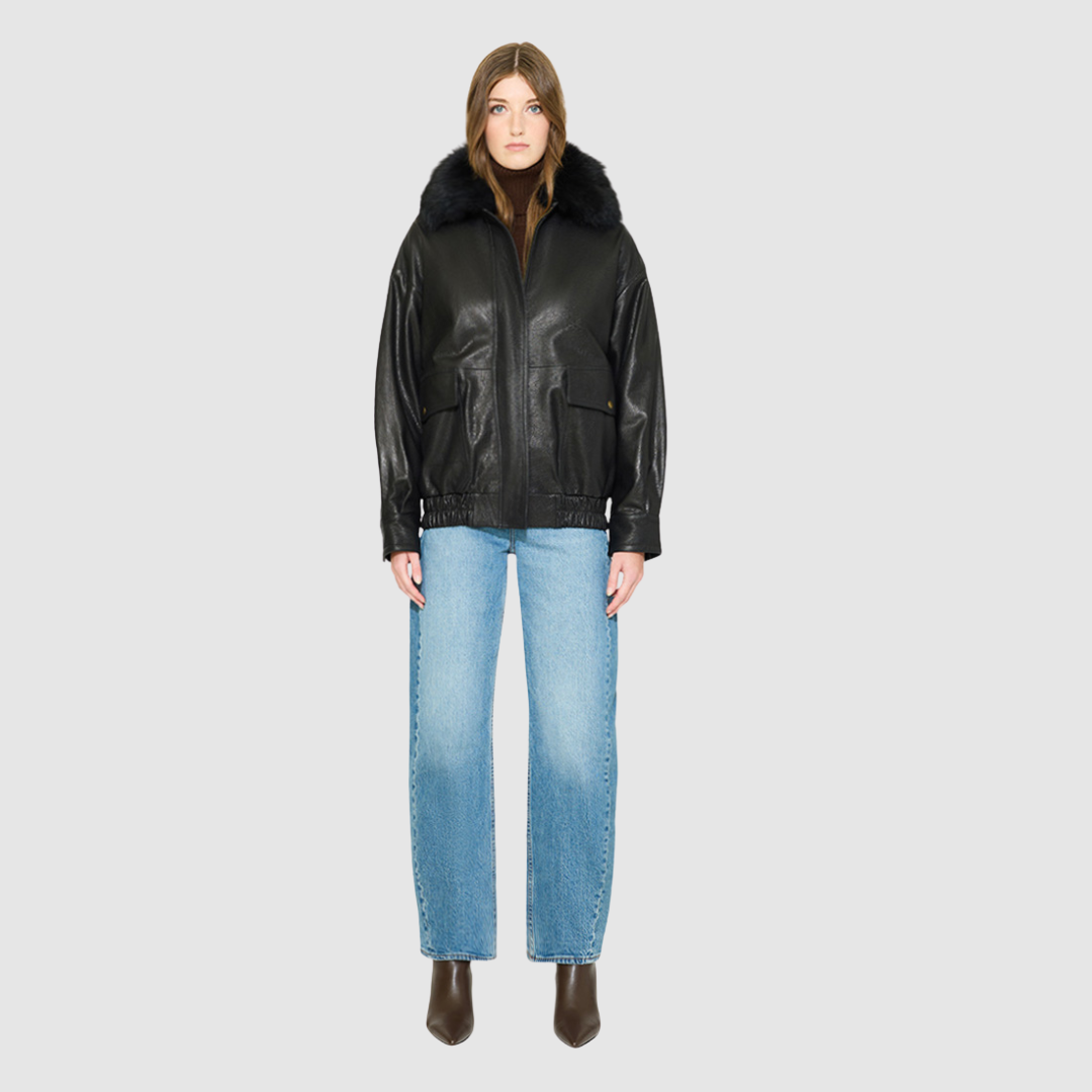 The TATE Bomber Jacket is a modern silhouette crafted in premium textured black leather. Designed with drop shoulders and a relaxed fit through the body, it delivers architectural volume and an easy, fluid drape. A dramatic, plush shearling collar and concealed front zip closure give it a clean, minimalist finish, while flap patch pockets and a gathered elasticized leather hem define the silhouette. Fully lined for comfort, TATE serves as a definitive statement piece for elevated cold-weather layering.