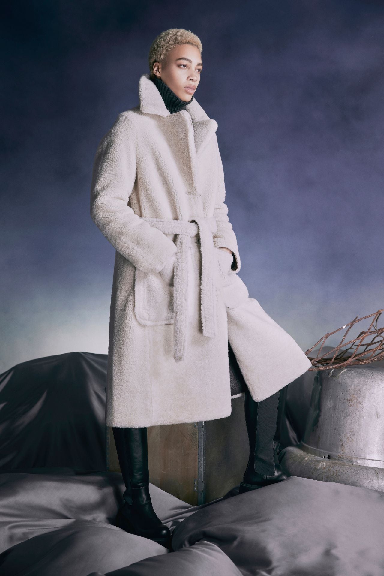 Introducing Zira, a vintage-inspired reversible notch collar nappa coat, perfect for winter. This versatile piece effortlessly transforms from classic nappa to cozy curly wool teddy, offering two looks in one. With a relaxed dropped shoulder silhouette and 3-button closure, it exudes timeless elegance. Complete with a tie belt at the waist and zip pockets on the nappa side, reversing to patch pockets on the teddy side, Zira is the ultimate outerwear essential for style and warmth. 51" long.